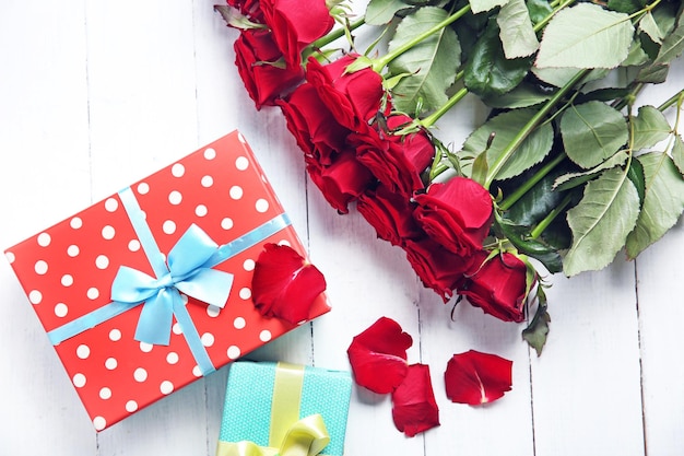 Beautiful bouquet of red roses and present boxes on wooden background