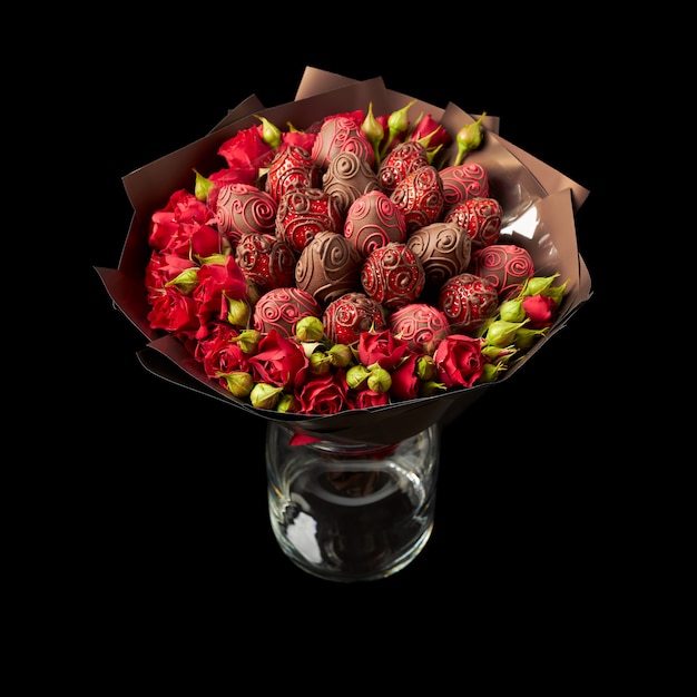 Beautiful bouquet of red roses and ripe strawberries in chocolate wrapped in brown paper on a black surface