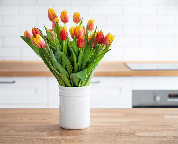 A beautiful bouquet of red and yellow tulips in a white vase on a wooden countertop against a white kitchen background Spring time concept Copy space