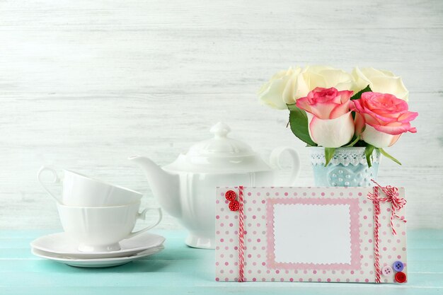 Beautiful bouquet of roses and handmade postcard on light wooden background