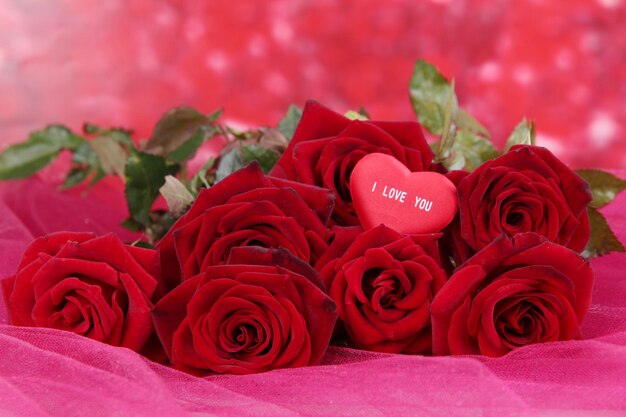 Photo beautiful bouquet of roses on pink fabric on red background