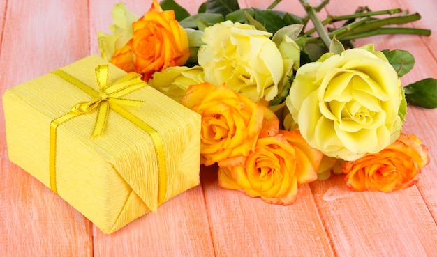 Beautiful bouquet of roses with gift on table close-up