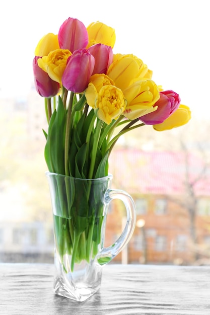 Beautiful bouquet of tulips in carafe on windowsill