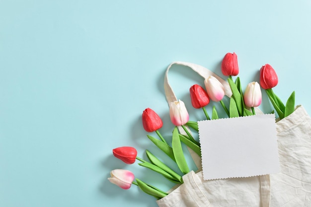 A beautiful bouquet of tulips in an eco bag on a light blue background International Women's Day March 8 Mother's Day Easter birthday Space for copying Flat position top view