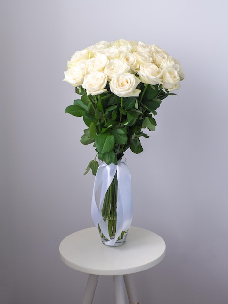 Beautiful bouquet of white blooming roses in glass vase on round table