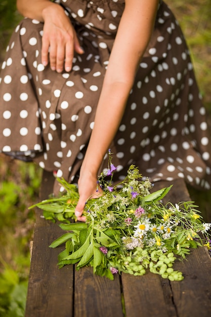 Красивый букет полевых летних цветов в женских руках на деревянном фоне