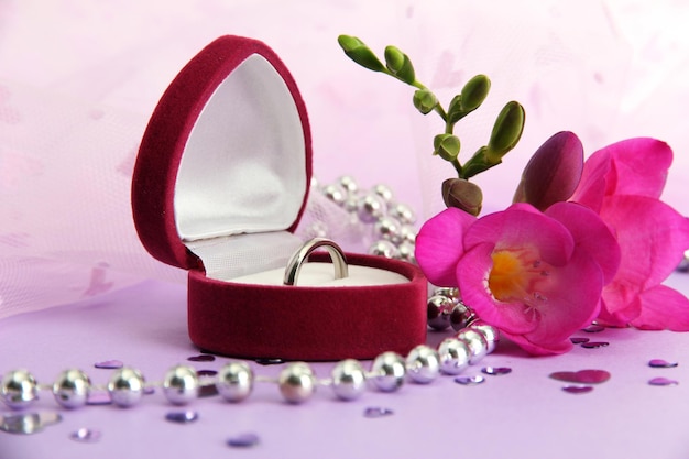 Beautiful box with wedding ring and flower on purple background