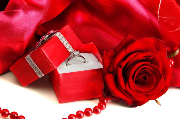 빨간 실크 배경에 결혼 반지와 장미가 있는 아름다운 상자