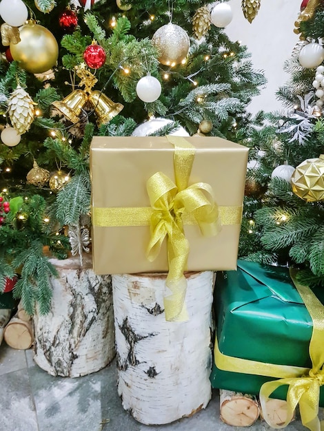 Beautiful boxes wrapped in gold paper with Christmas gifts on a birch stump near the Christmas tree