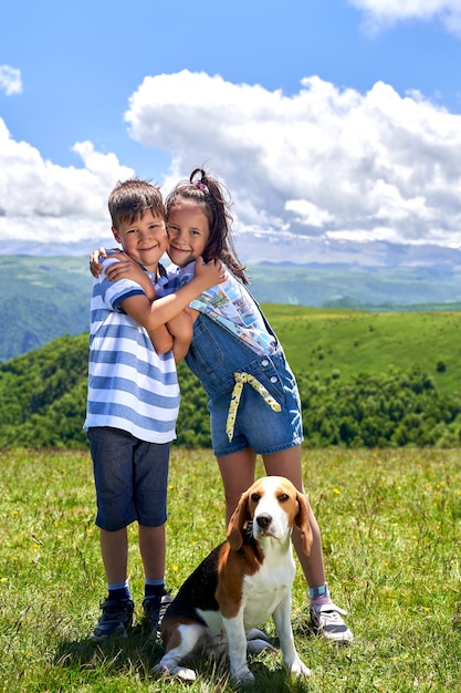 Beautiful boy and girl with a dog on the background of mountains.