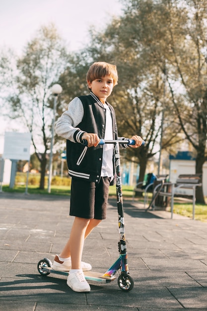 Foto un bel ragazzo guida uno scooter nel parco. il bambino trascorre un tempo attivo all'aria aperta.