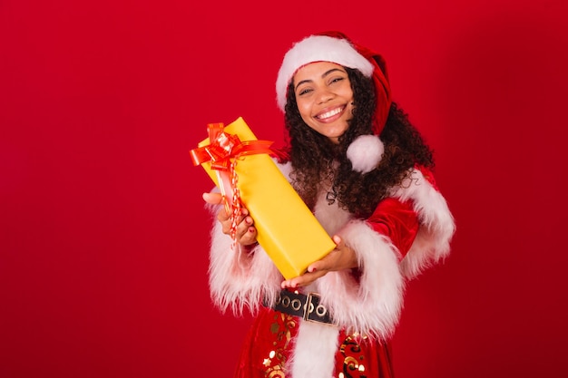 Beautiful brazilian black woman dressed as santa claus christmas clothes gifting someone with yellow gift