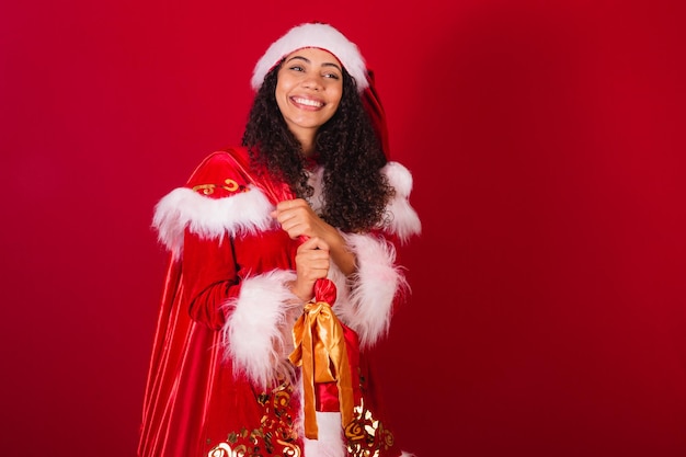 Beautiful brazilian black woman dressed as santa claus christmas clothes holding santa's bag smiling