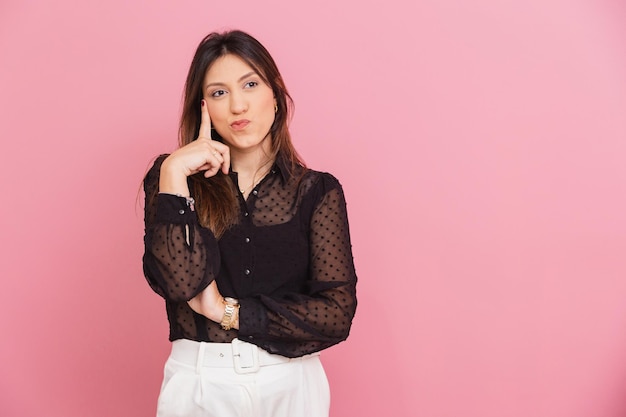 Beautiful Brazilian Caucasian Woman Pink Background Doubtful Look With Finger on Cheek Thinking Doubting Questioning Thinking Expression