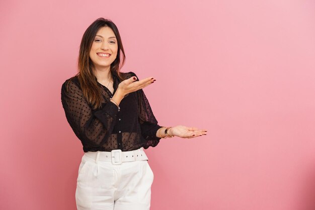 Beautiful Brazilian Caucasian Woman Pink Background Smiling Receptive Presenting and Indicating Suggesting a Product or Advertisement by Her Side ad negative space