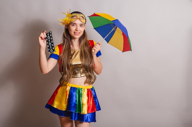 Beautiful brazilian caucasian woman wearing frevo carnival\
clothes wearing a mask holding condom prevention