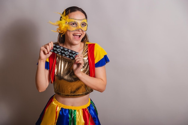 Beautiful brazilian caucasian woman wearing frevo carnival\
clothes wearing a mask holding condom prevention