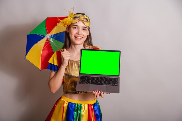 Beautiful brazilian caucasian woman wearing frevo carnival\
clothes wearing a mask holding notebook with green screen in\
chroma