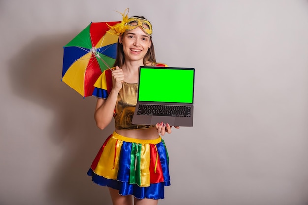 Beautiful brazilian caucasian woman wearing frevo carnival\
clothes wearing a mask holding notebook with green screen in\
chroma