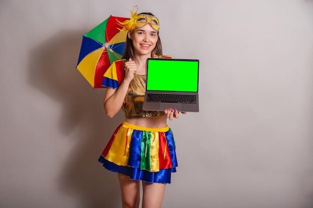 Beautiful brazilian caucasian woman wearing frevo carnival\
clothes wearing a mask holding notebook with green screen in\
chroma