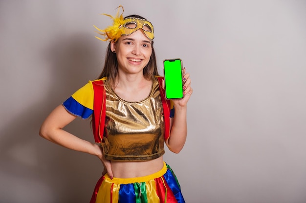 Beautiful brazilian caucasian woman wearing frevo carnival
clothes wearing a mask holding smartphone with green screen in
chroma