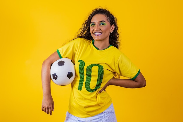 黄色の背景のワールドカップ2022にサッカーボールを持つ美しいブラジルの女性サポーター