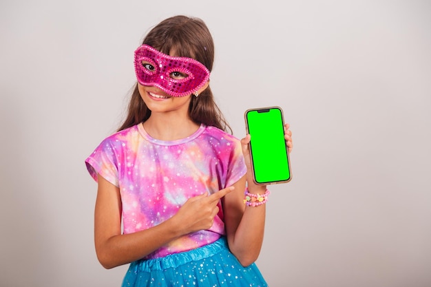 Beautiful Brazilian girl child dressed for carnival in Brazil showing smartphone with green Chroma screen