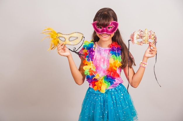 Beautiful Brazilian girl child dressed for carnival in Brazil with carnival mask holding masks inviting to party