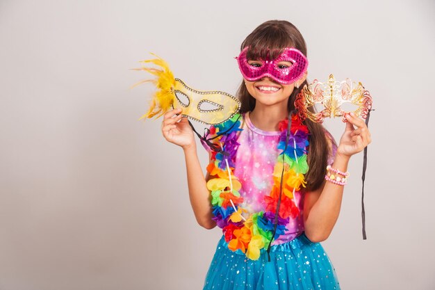 Beautiful Brazilian girl child dressed for carnival in Brazil with carnival mask holding masks inviting to party