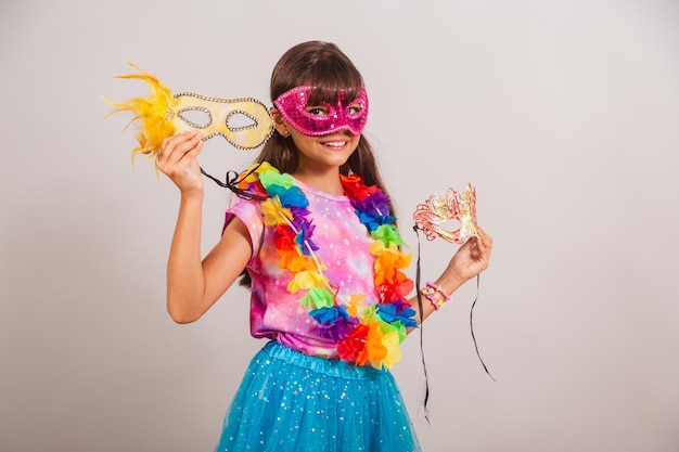 Beautiful brazilian girl child dressed for carnival in brazil\
with carnival mask holding masks inviting to party