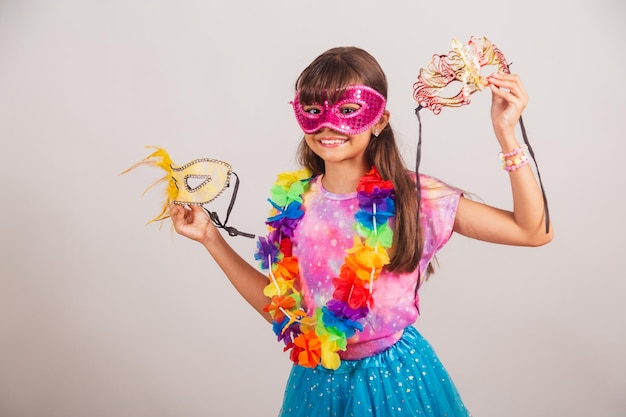 Beautiful brazilian girl child dressed for carnival in brazil\
with carnival mask holding masks inviting to party