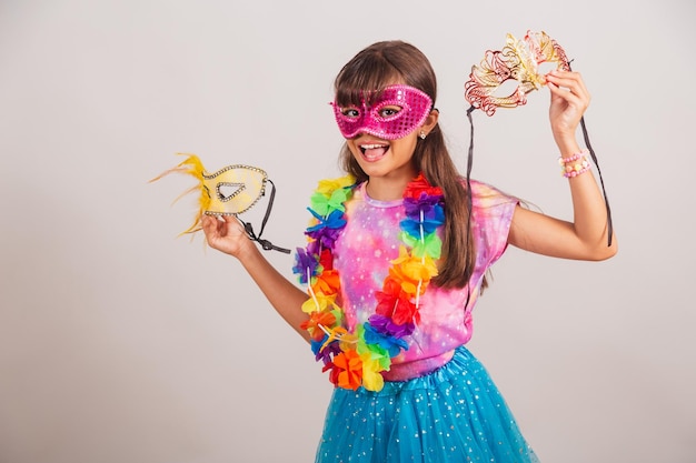 Beautiful brazilian girl child dressed for carnival in brazil\
with carnival mask holding masks inviting to party