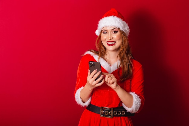 아름 다운 브라질 redhaired 여자 크리스마스 옷을 입고 산타 클로스 지주 스마트폰 입력
