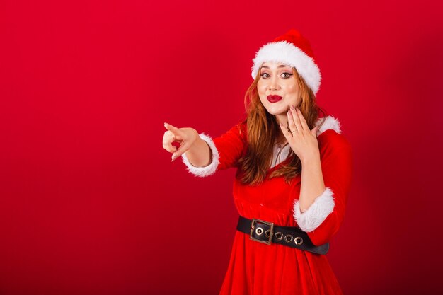 Beautiful brazilian redhaired woman dressed in christmas clothes santa claus pointing at something in the distance