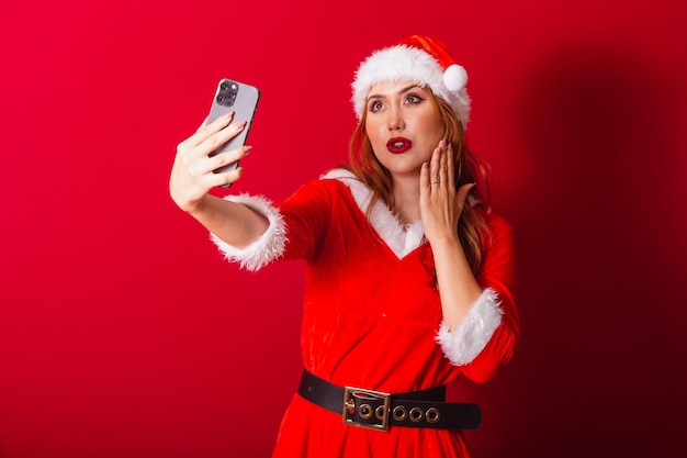 クリスマスの服を着た美しいブラジルの赤髪の女性サンタクロースがスマートフォンでビデオ通話