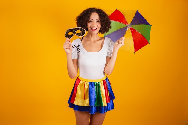 Beautiful Brazilian woman dressed in carnival clothes colorful skirt and white shirt frevo umbrella holding carnival mask