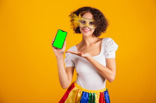 Beautiful Brazilian woman dressed in carnival clothes colorful skirt and white shirt holding smartphone and showing green screen in chroma