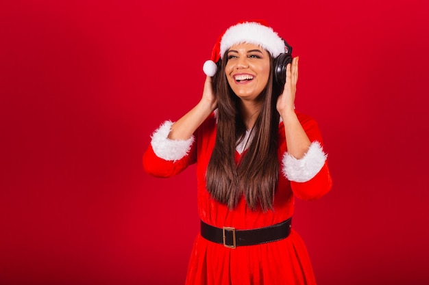 クリスマスの服を着た美しいブラジル人女性サンタクロースがヘッドセットで音楽を聴く