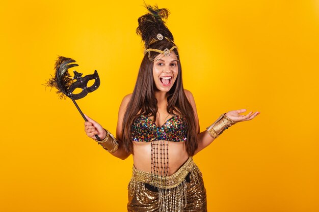 Beautiful brazilian woman in golden carnival clothes holding carnival mask as well