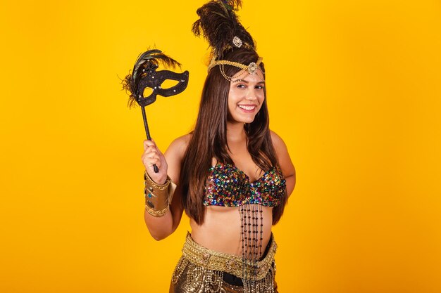 Beautiful brazilian woman in golden carnival clothes holding carnival mask