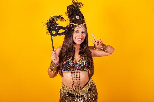 Beautiful brazilian woman in golden carnival clothes putting on carnival mask taking portrait portrait