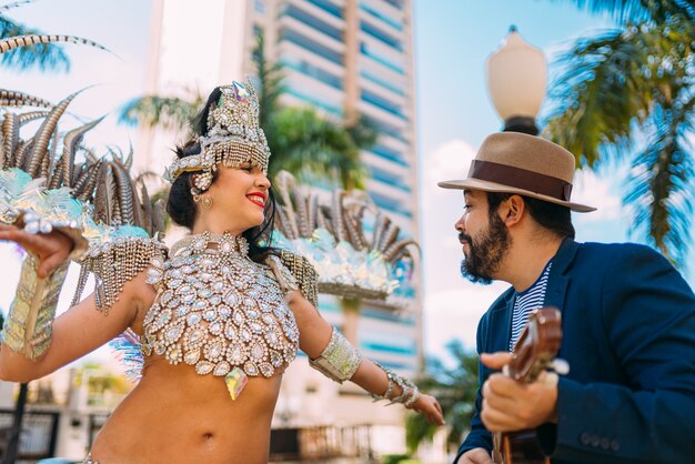 Beautiful brazilian woman wearing colorful carnival costume and\
a samba player playing brazilian instrument during carnaval street\
parade in city.