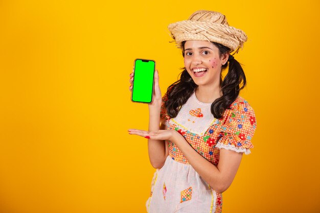 Photo beautiful brazilian woman with festa junina clothes holding smartphone with green screen