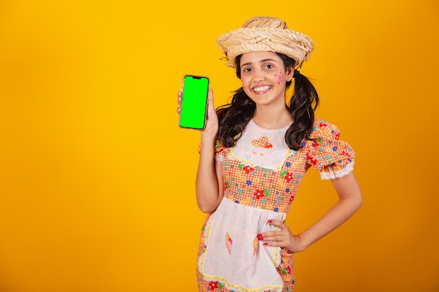 Beautiful Brazilian woman with festa junina clothes holding smartphone with green screen