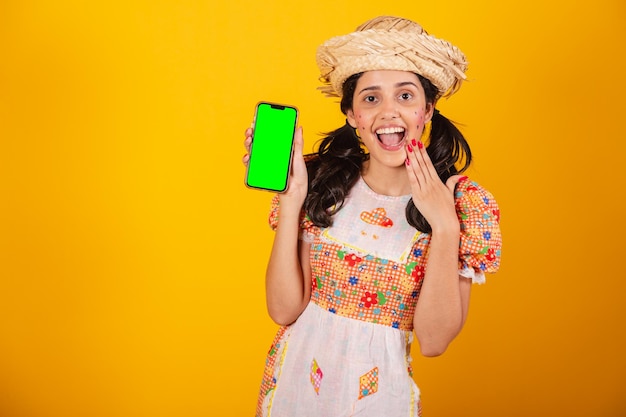 Beautiful Brazilian woman with festa junina clothes holding smartphone with green screen