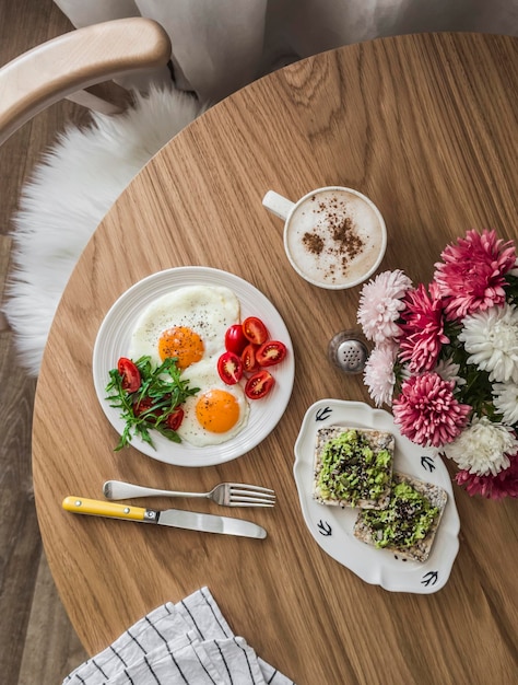 A beautiful breakfast served on a wooden table eggs arugula cherry tomatoes salad bread with avocado and flax seeds coffee Top view