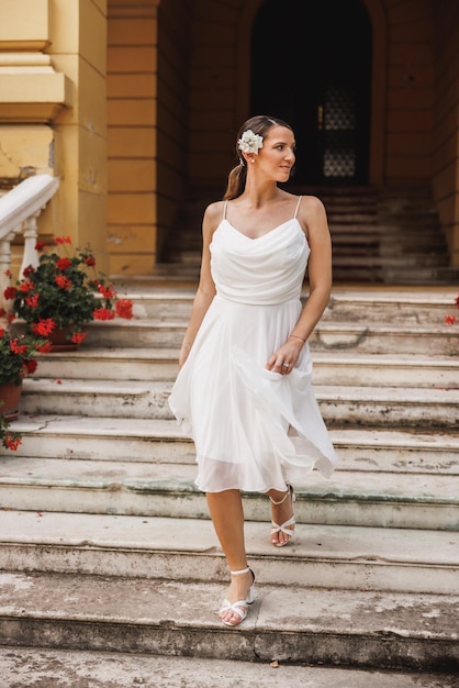 아름다운 하얀 웨딩드레스를 입은 아름다운 신부가 결혼식 날 야외 계단을 걸어 내려갑니다.