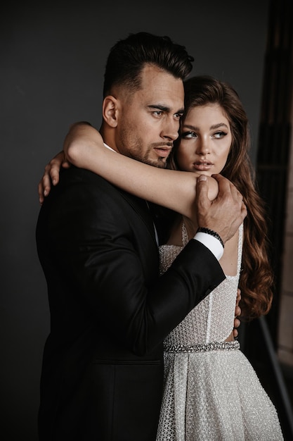 Beautiful bride and elegant groom on black background. Stylish newlywed couple. Marriage concept