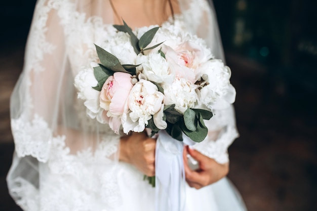 Beautiful bride holds in her hands a wedding bouquet with peonies.