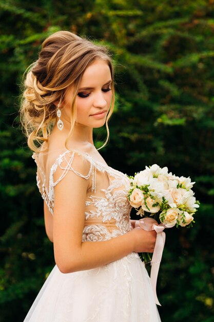 Beautiful bride holds a wedding bouquet on the background of green trees